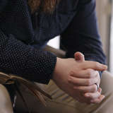 A man is sitting with an open Bible, hands folded in prayer